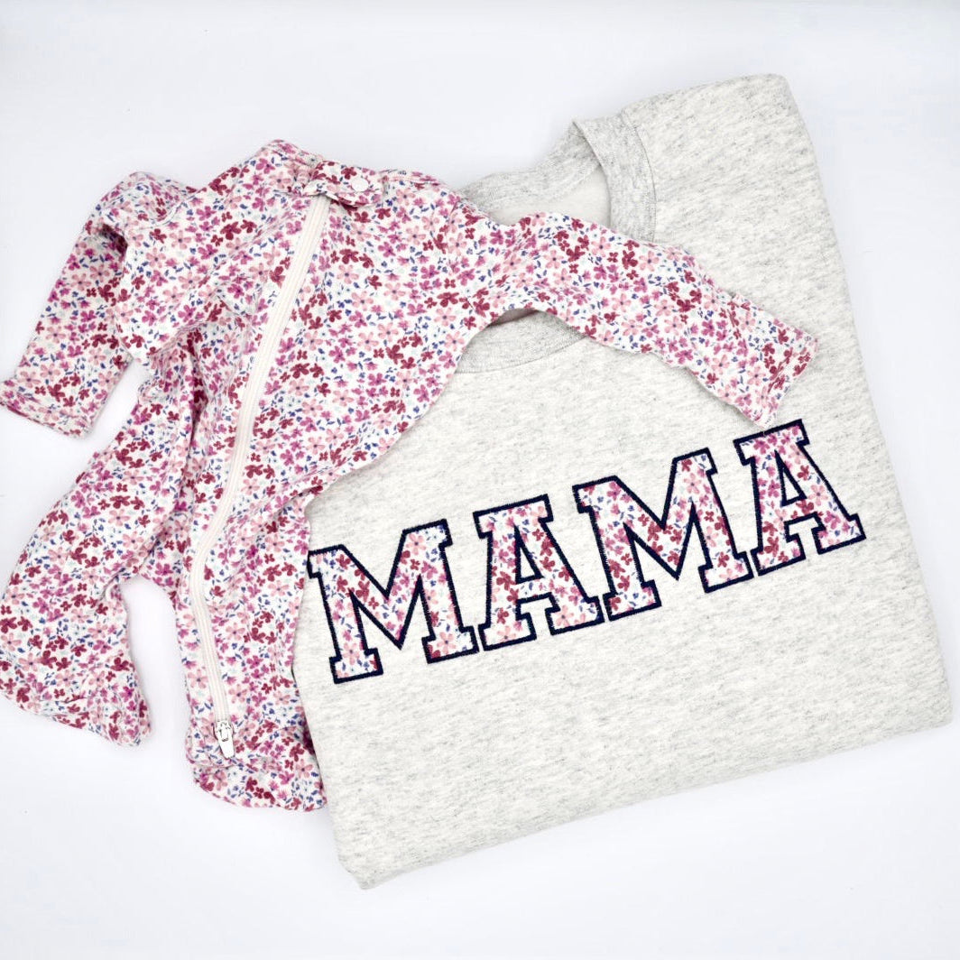Ash sweatshirt with the word "MAMA" in large outlined letters, layered over a matching long-sleeve baby romper with a pink, red, and white floral print, laid flat on a white background.